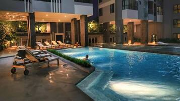 An outdoor swimming pool with lounge chairs and a poolside cart, surrounded by modern buildings.