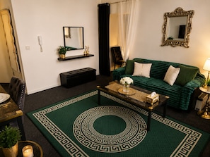 Een woonkamer met een groene bank, een bijzettafeltje, een spiegel, een telefoon en een decoratief vloerkleed.