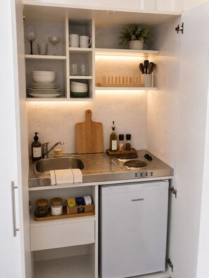 Eine kompakte Küche mit Spüle, kleinem Kühlschrank und Schneidebrett.