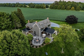 A large house with a deck, surrounded by lush greenery and a field.