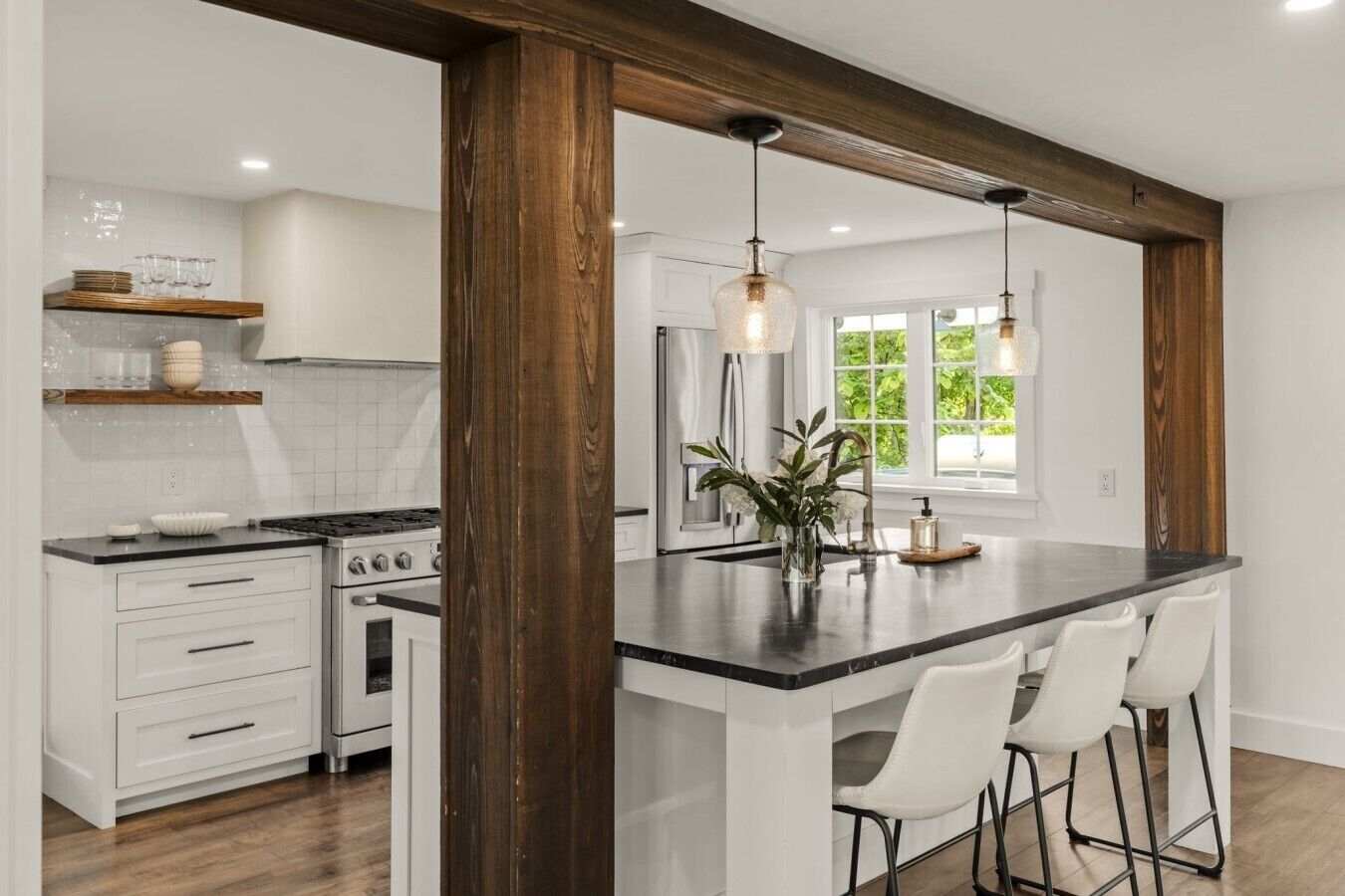 Une cuisine moderne avec des meubles blancs, un îlot central doté de tabourets et des luminaires suspendus.