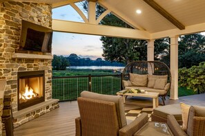 A covered outdoor seating area with a stone fireplace, wicker furniture, and a view of a lake. - Welcome to the magic of Langford Creek Farm (Chestertown)