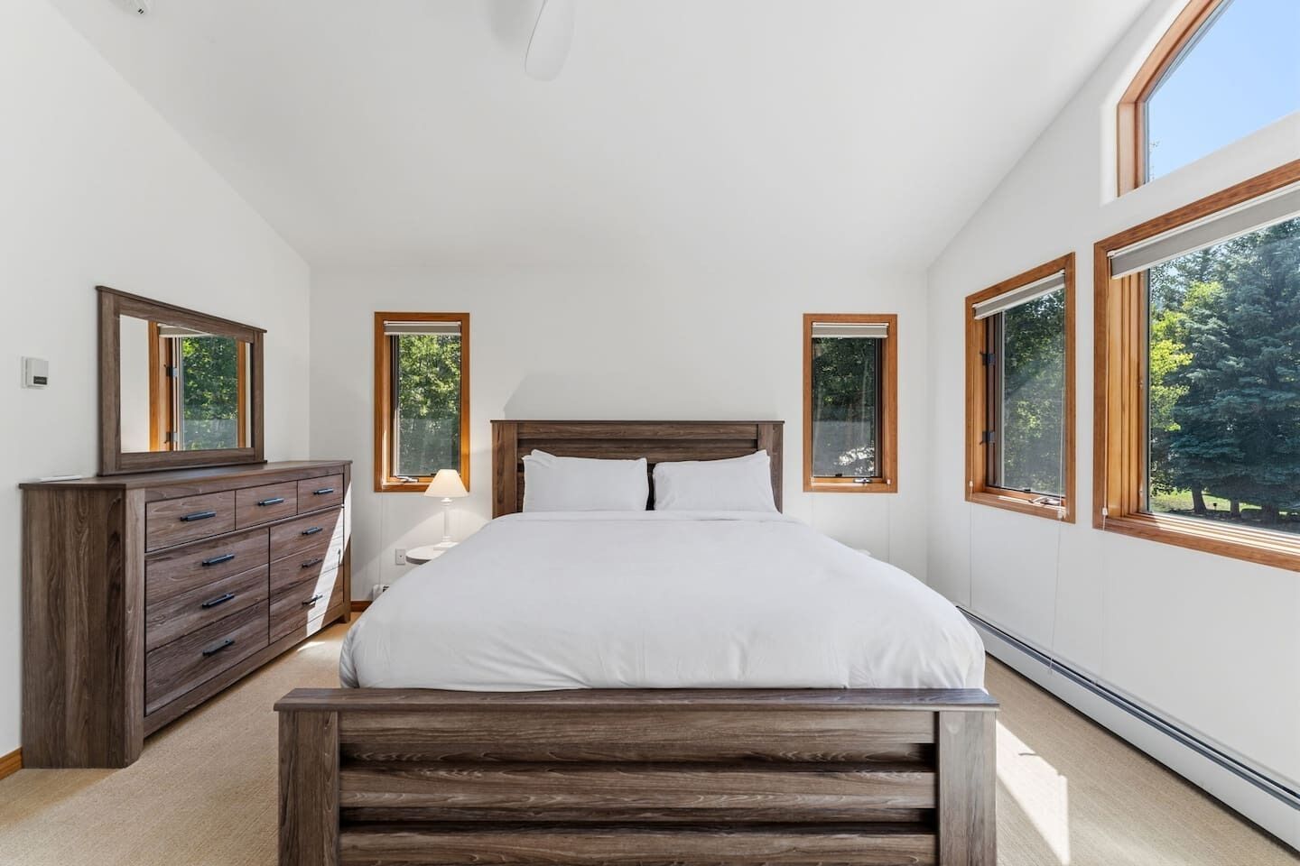 A bedroom with a large bed, wooden headboard, a dresser, and multiple windows providing natural light.