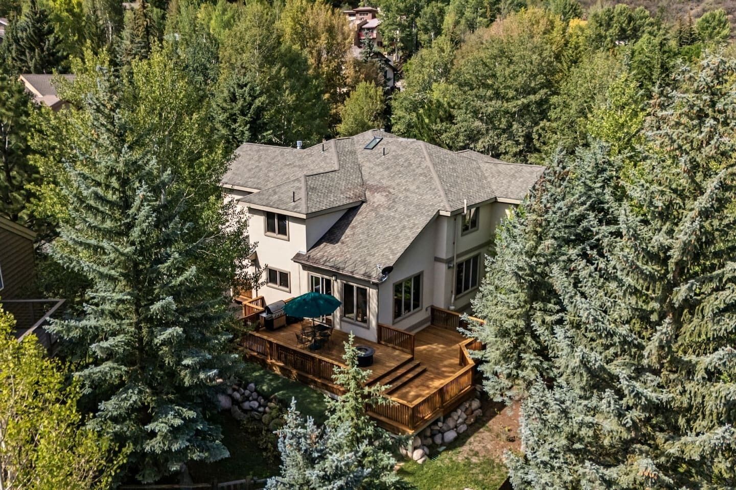 A two-story house with a deck, surrounded by dense evergreen trees.