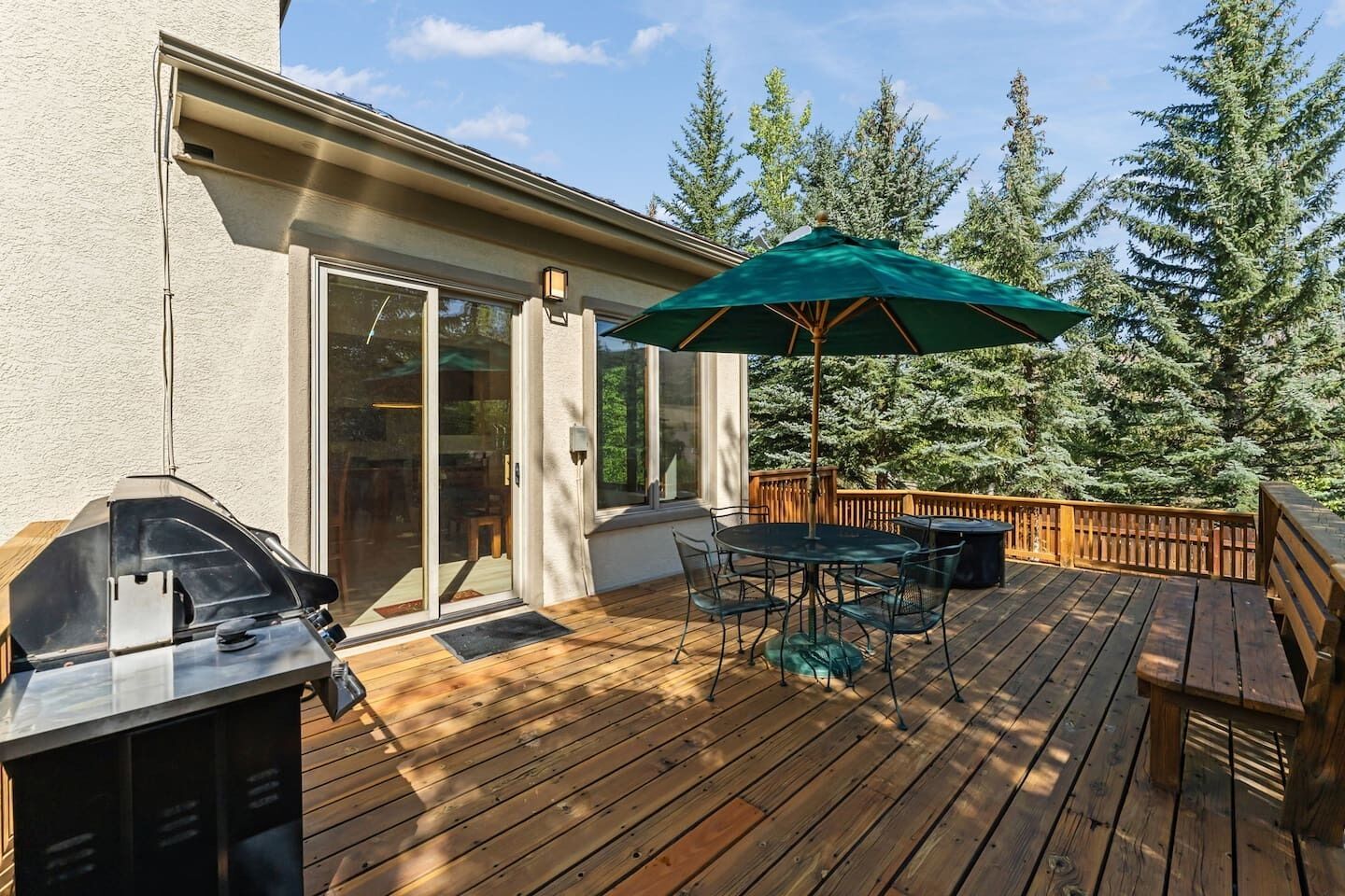 A wooden deck with a barbecue grill, a table with chairs, and a green umbrella.