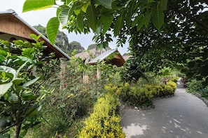 Um caminho leva a um edifício de madeira rodeado por vegetação exuberante e plantas floridas.