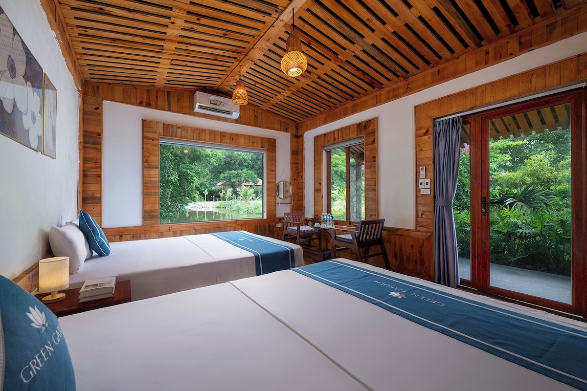 A room with two beds, a desk, and a view of greenery.
