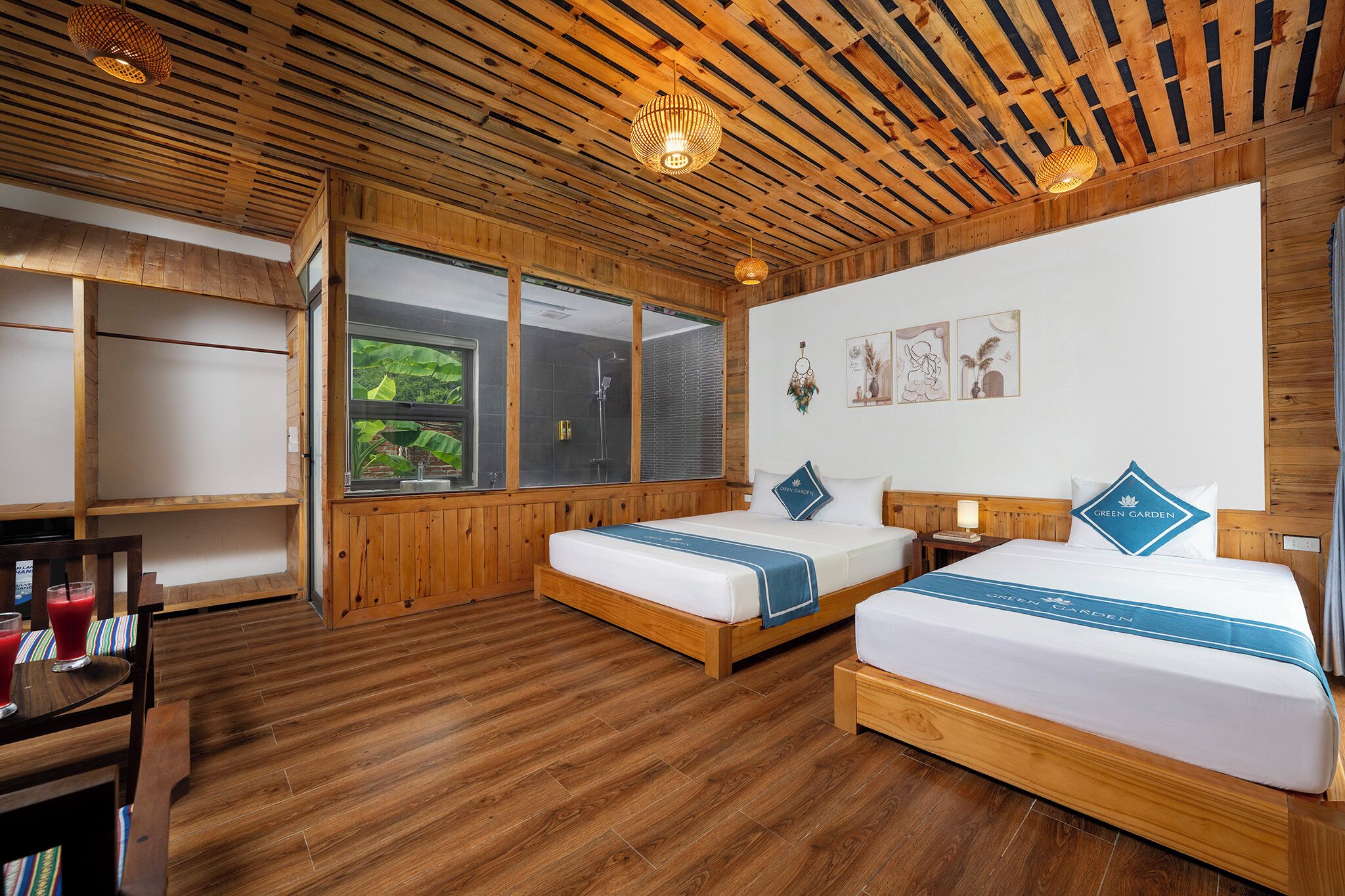 Quarto de hotel com decoração em madeira, duas camas, chuveiro e área de refeições.