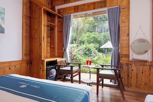 Una habitación de madera con una cama, una mesa, sillas, un refrigerador pequeño y un ventanal con cortinas.
