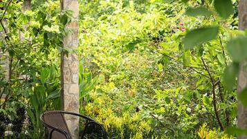 A covered outdoor seating area with a chair, surrounded by lush greenery and a stone pillar.