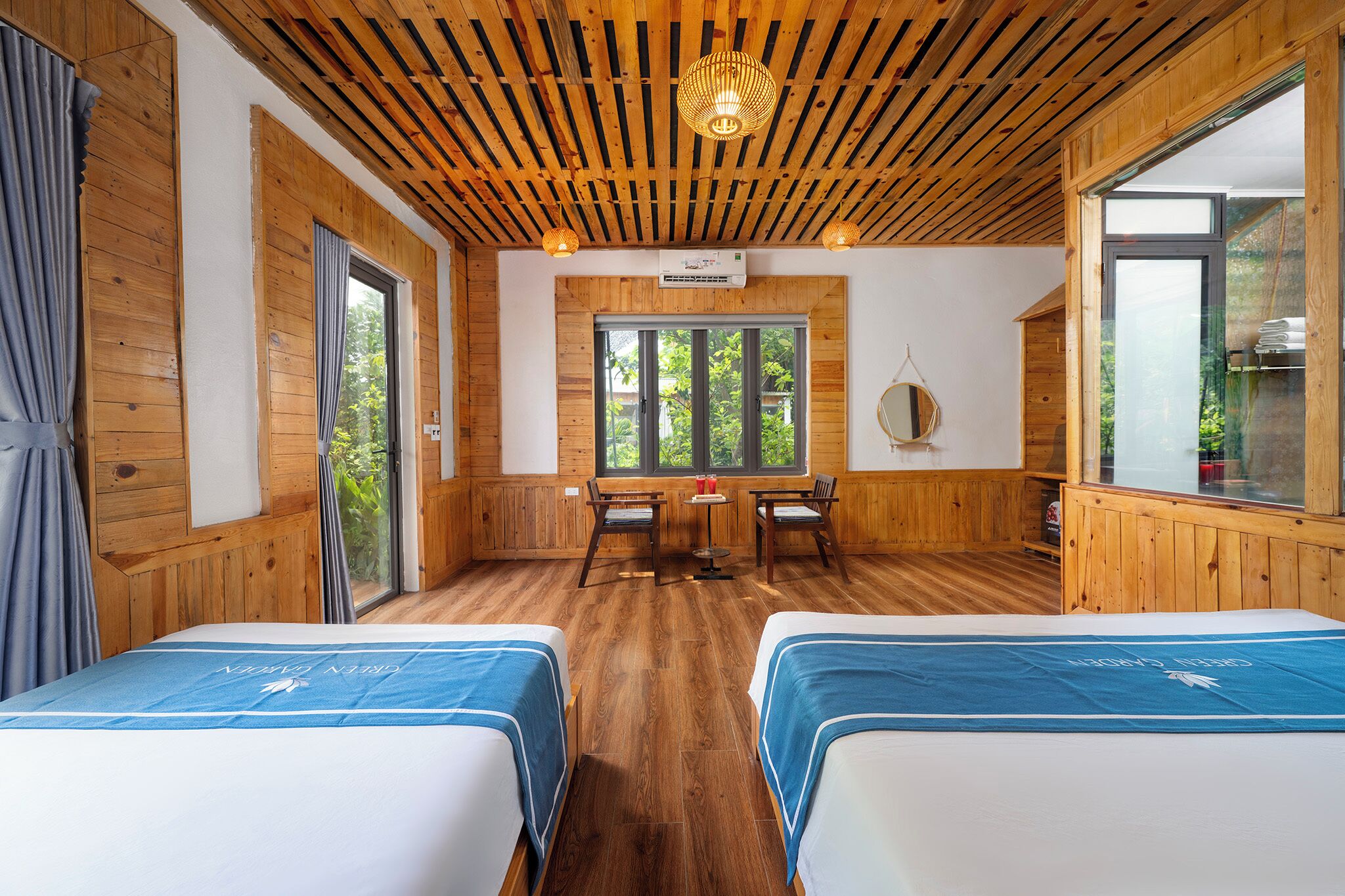 A room with two beds, a wooden ceiling, a dining table with chairs, and a large window.