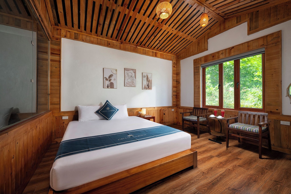 A wooden room with a large bed, a window with a view, and a small table with chairs.