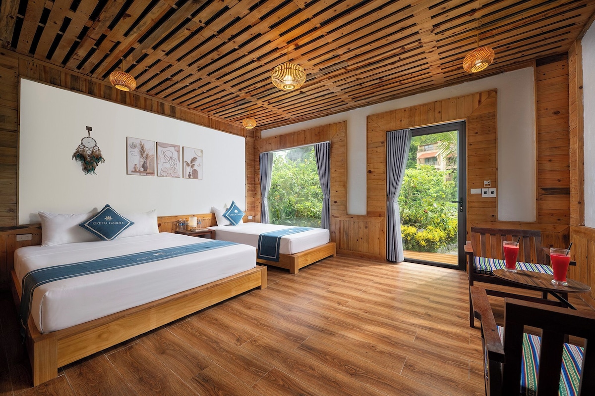 A room with two beds, wooden flooring, a dining area with a table and chairs, and a view through a glass door.