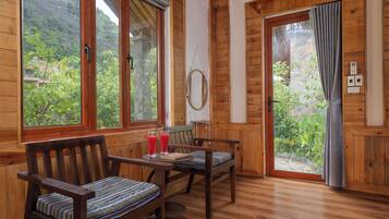 A wooden interior with a dining table and chairs, a window with a view of greenery, and a door with a curtain.