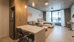 Een moderne keuken met een koelkast, een eettafel met stoelen, een bank en een bed op de achtergrond.