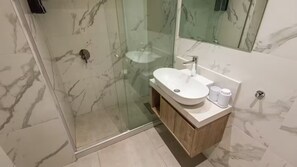 Een moderne badkamer met een douchecabine van glas, een betegelde wand van marmer en een houten wastafelmeubel met een wastafel en spiegel.