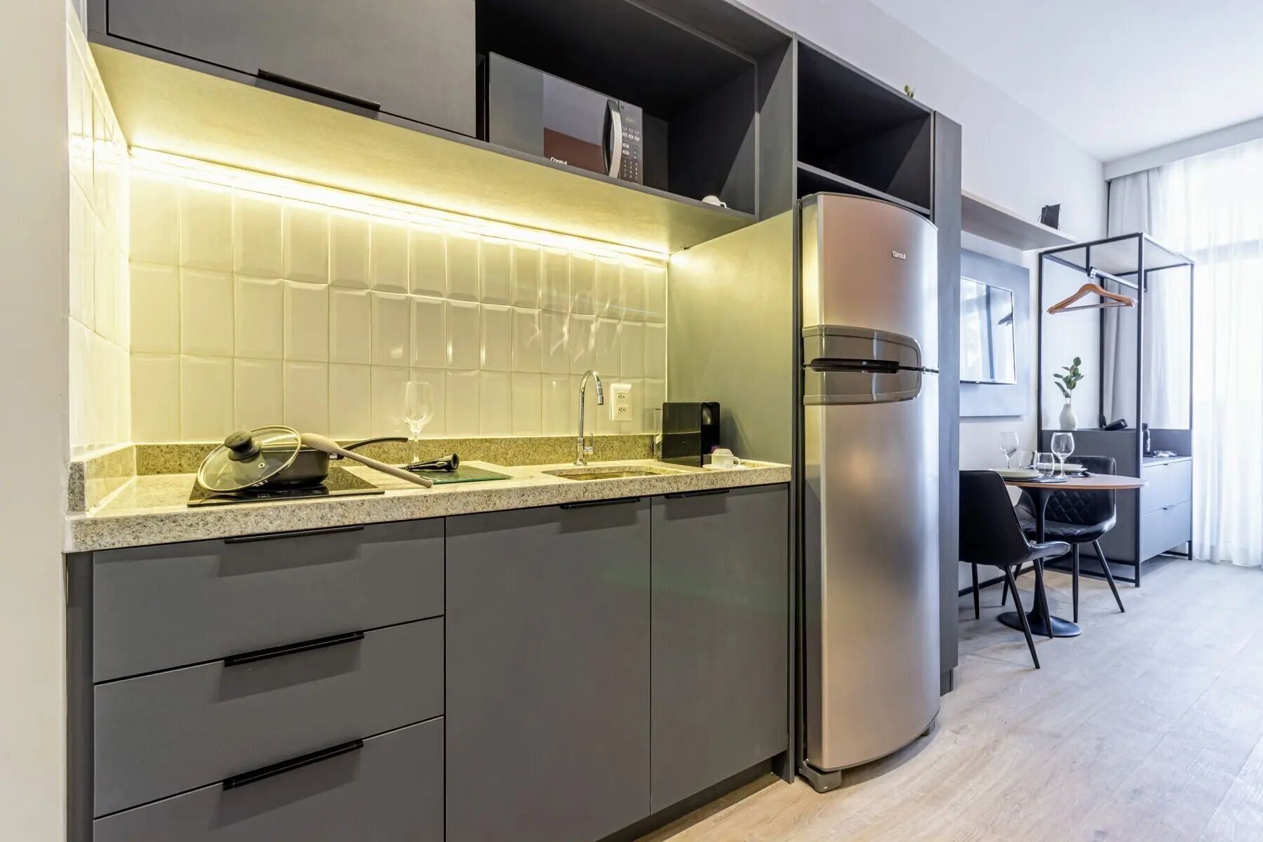 A modern kitchen with a built-in microwave, a stainless steel refrigerator, and a countertop with a kettle and a wine glass.