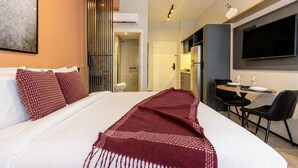 A hotel room with a bed, a desk with chairs, a television, and a bathroom. - Arte Onze de Junho (São Paulo)
