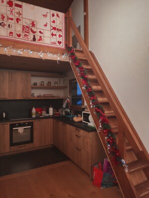 Eine Küche mit Holzschränken, einer Mikrowelle und einer Holztreppe mit roter und grüner Girlande.