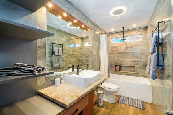 A modern bathroom with a marble sink, a glass shower enclosure, and a wooden vanity.