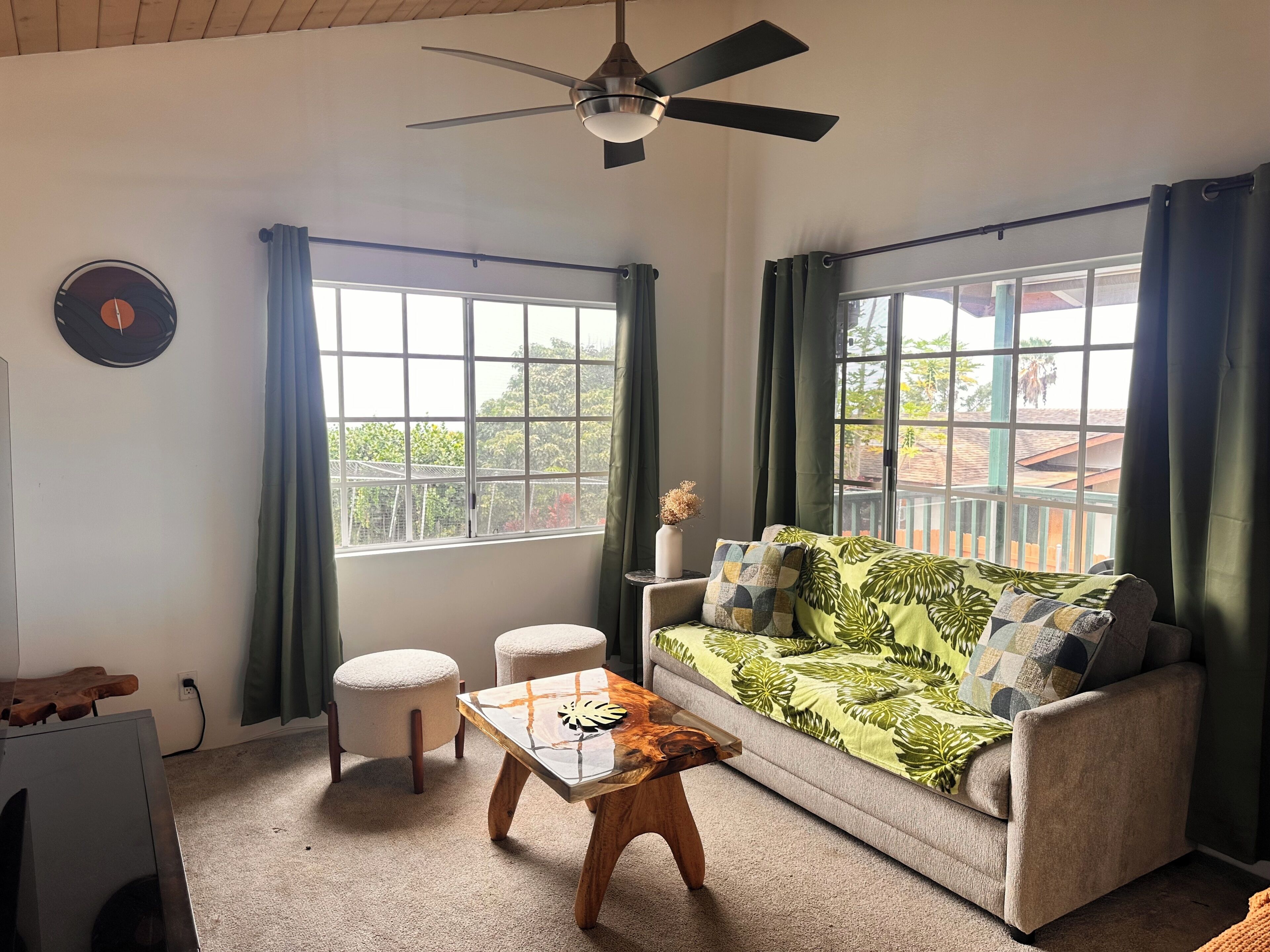 A living room with a ceiling fan, a sofa with patterned cushions, a coffee table, and two ottomans.