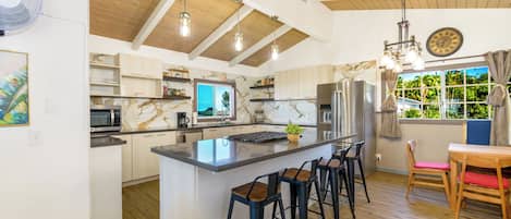 A modern kitchen with a central island, bar stools, and a dining area with a view.