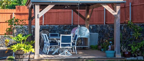 A covered outdoor patio with a grill, seating area, and stone wall backdrop.