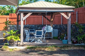 A covered outdoor patio with a grill, seating area, and stone wall backdrop.