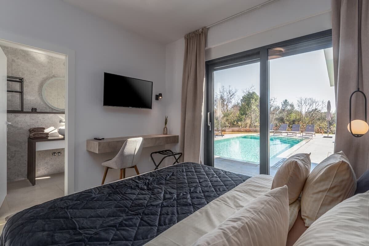 Habitación de hotel con cama, televisión, escritorio y vista a una piscina al aire libre.