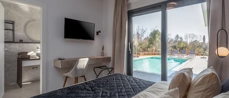 Habitación de hotel con cama, televisión, escritorio y vista a una piscina al aire libre.