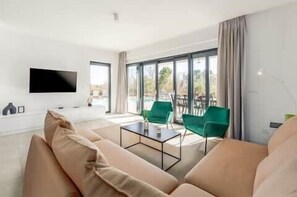 Una sala de estar moderna con televisor de pantalla plana, sofá, mesa de centro y vista al exterior.