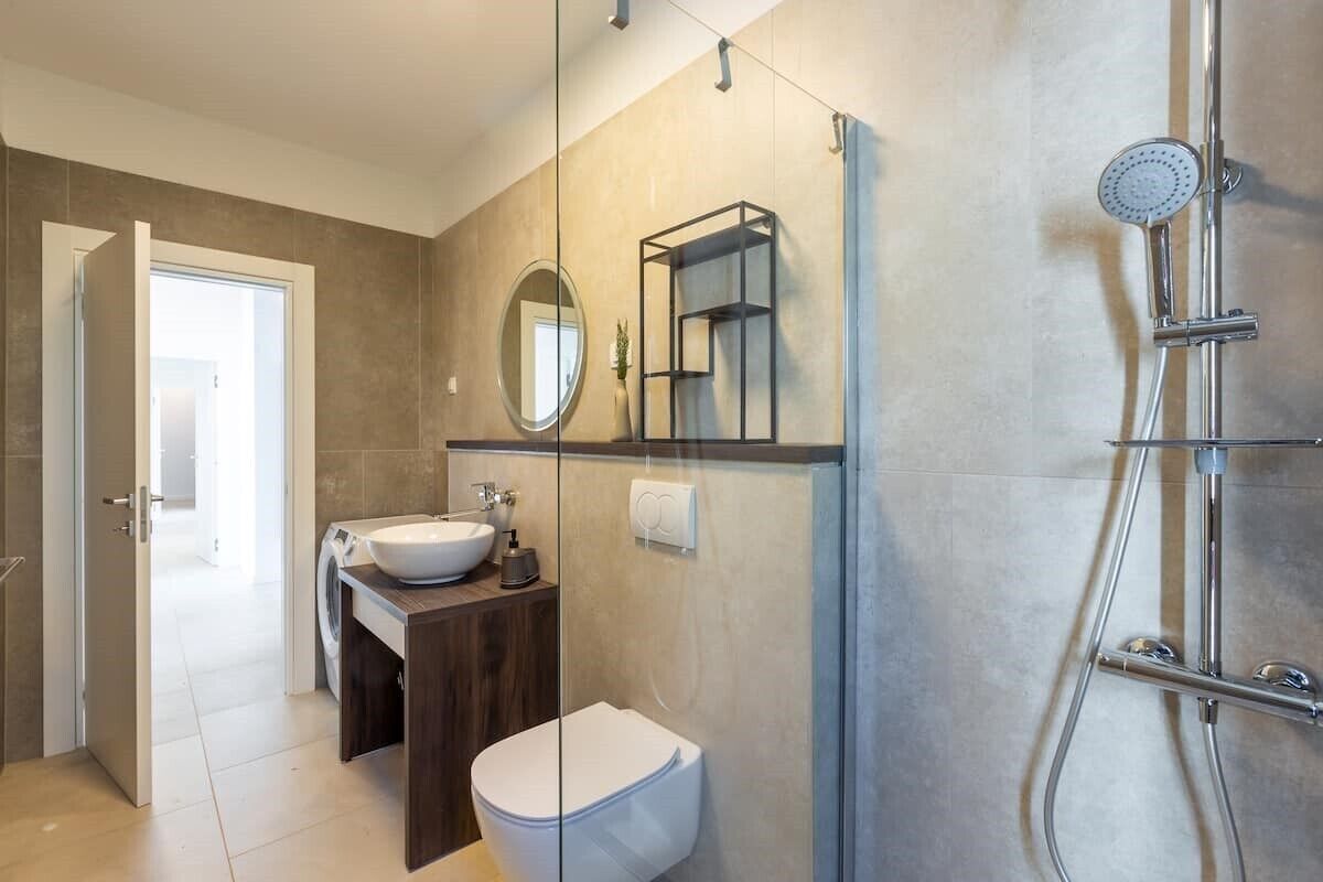 A modern bathroom with a glass shower enclosure, a white sink, and a toilet.