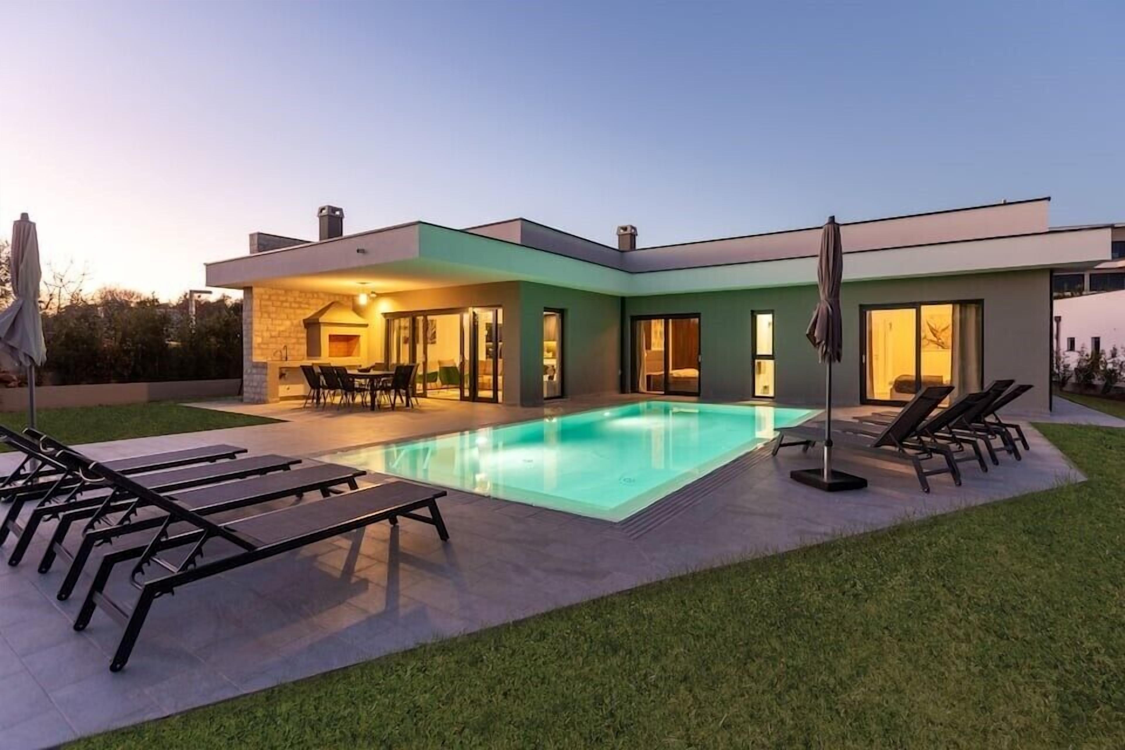 A modern house with a swimming pool, outdoor seating, and a well-maintained lawn.