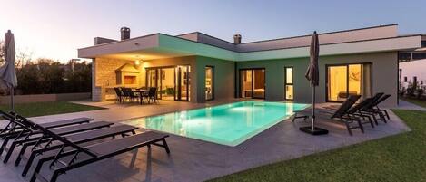 A modern house with a swimming pool, outdoor seating, and a well-maintained lawn.