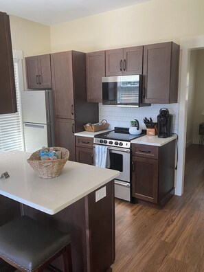 Una cocina con armarios de madera oscura, un refrigerador de acero inoxidable, un microondas, un horno y una cafetera sobre la encimera.