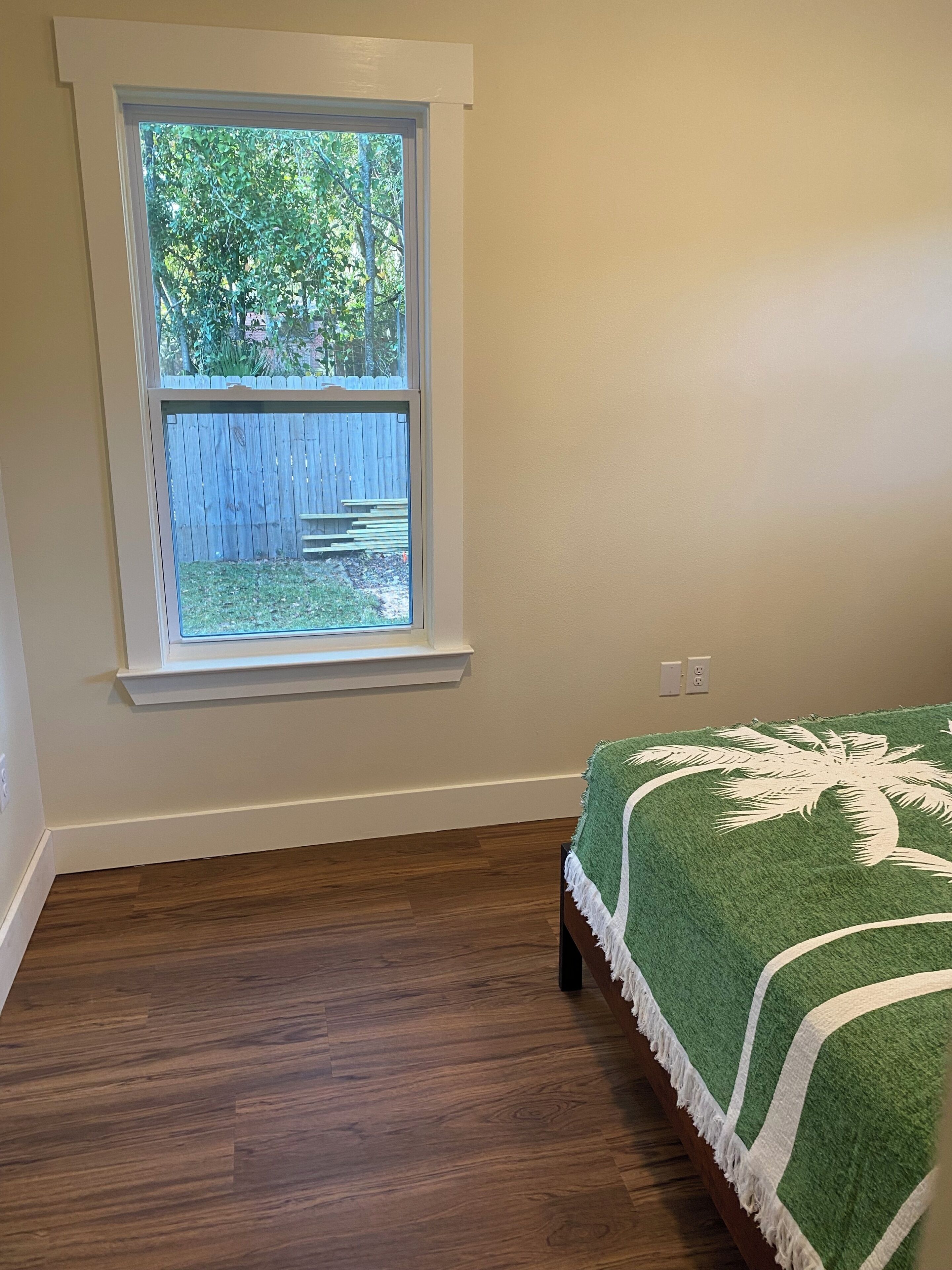 A bedroom with a window, wooden flooring, and a bed with a green blanket.