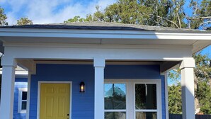 Uma casa com fachada azul, uma porta amarela e duas cadeiras Adirondack amarelas no alpendre.
