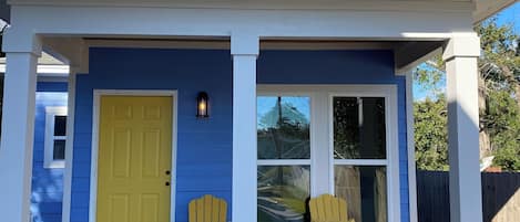 A house with a blue exterior, a yellow door, and two yellow Adirondack chairs on the porch.