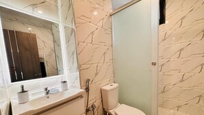 Et badeværelse med en marmorvæg, toilet, vask med spejl og en bruseafdeling.