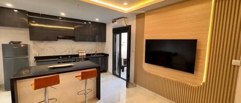 A modern kitchen with a central island, bar stools, and a flat-screen TV mounted on the wall.