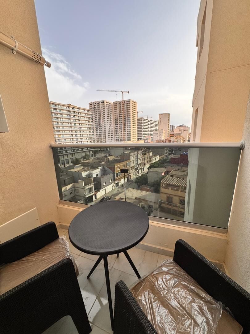 Un balcon doté d’une balustrade en verre, d’une table ronde et de deux chaises en osier.