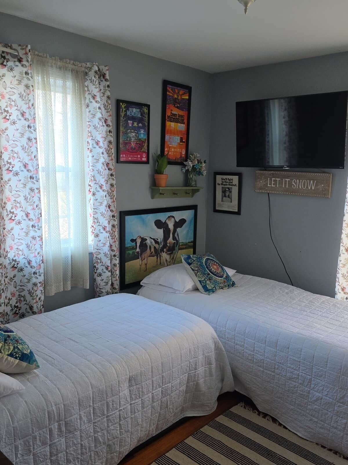 A bedroom with two beds, a TV, and various wall decorations including posters and a sign.