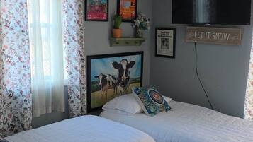 A bedroom with two beds, a TV, and various wall decorations including posters and a sign.