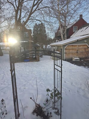 A residential area with a snow-covered yard, a wooden fence, and houses with visible chimneys.