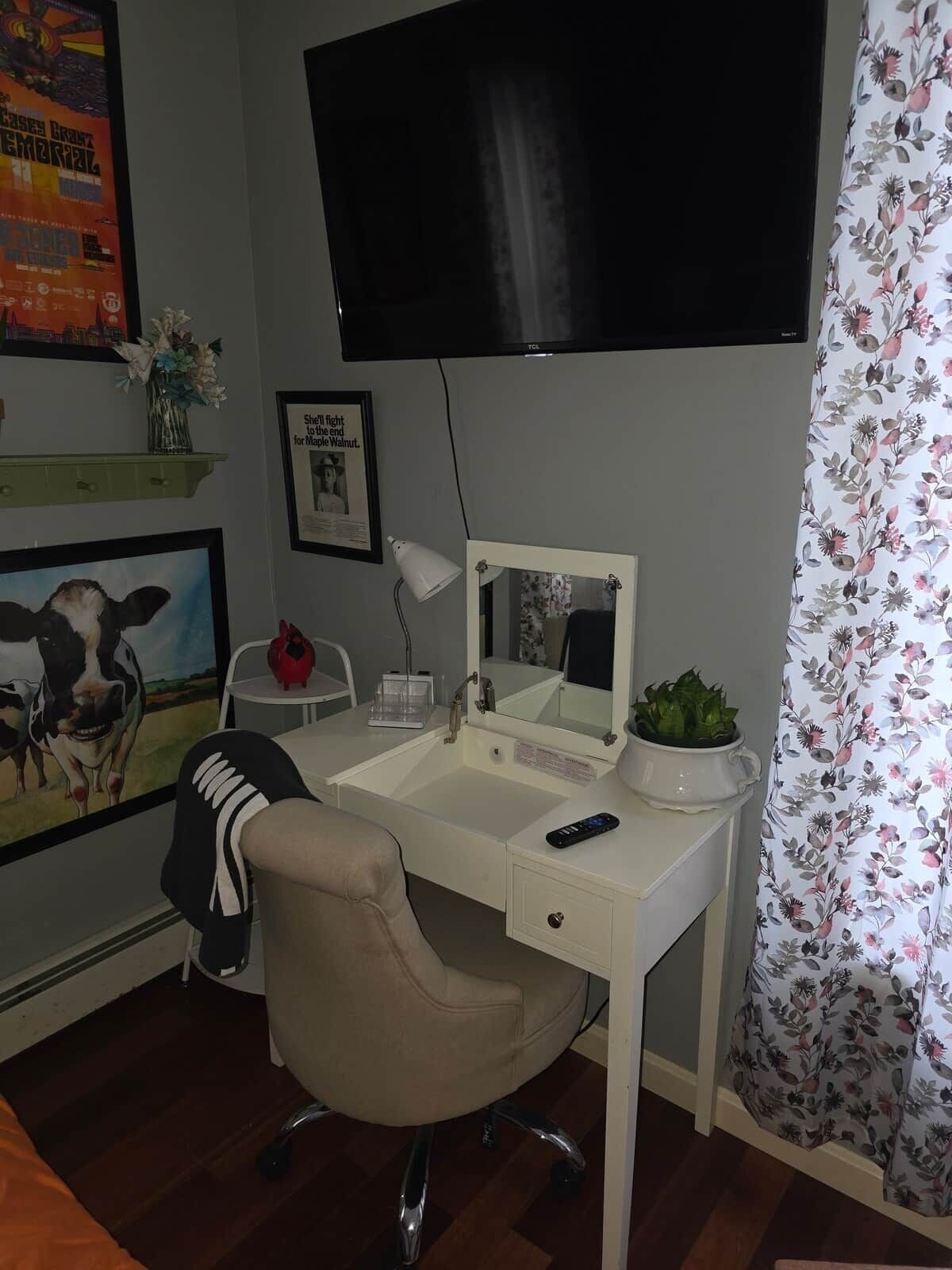 A room with a desk, chair, TV, and a mirror.