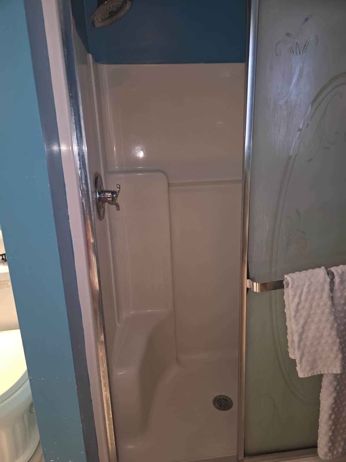A bathroom with a shower enclosure, a towel rack with a towel, and a toilet.