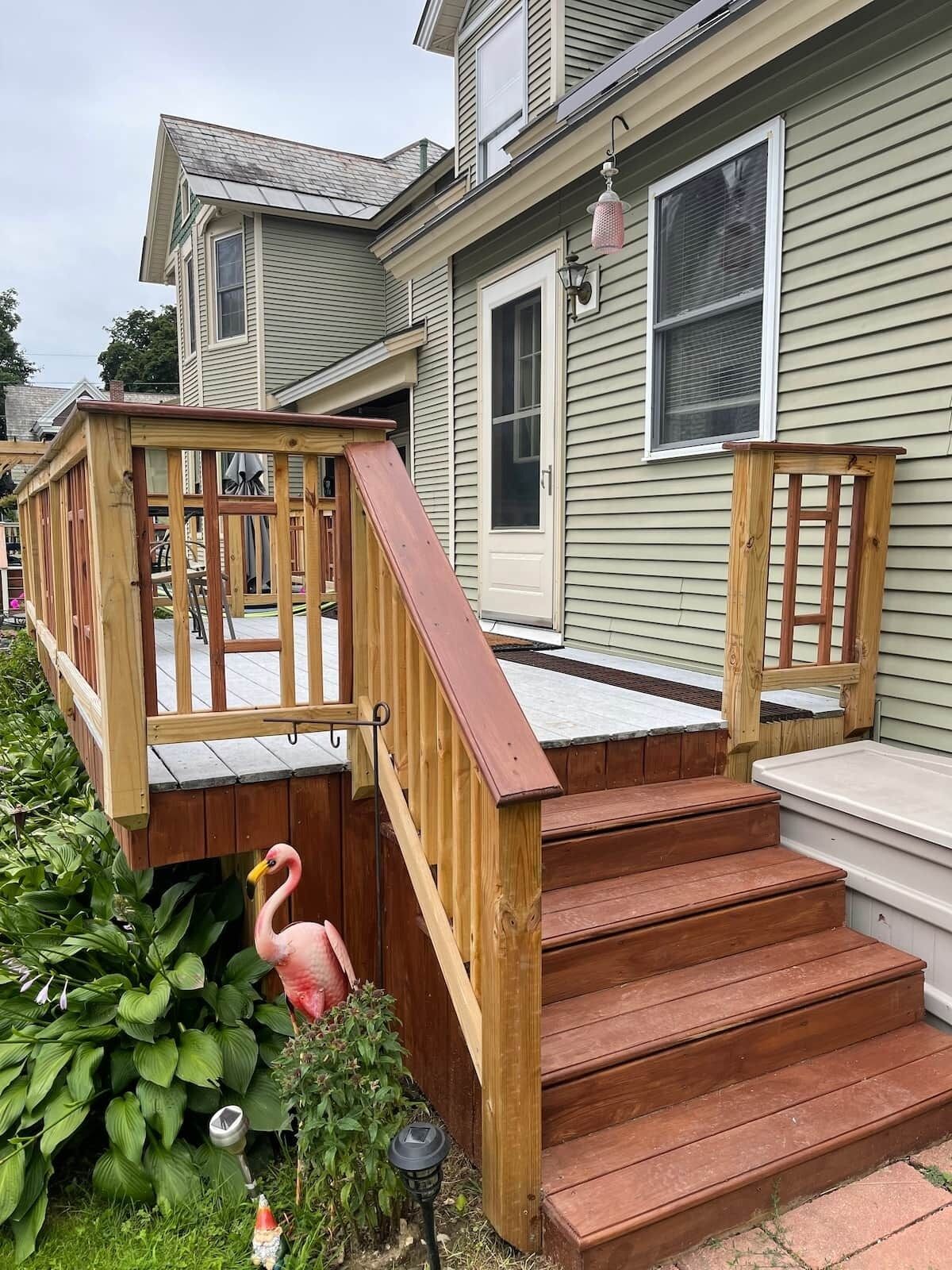 A house with a wooden deck, a pink flamingo decoration, and a small garden with green plants.