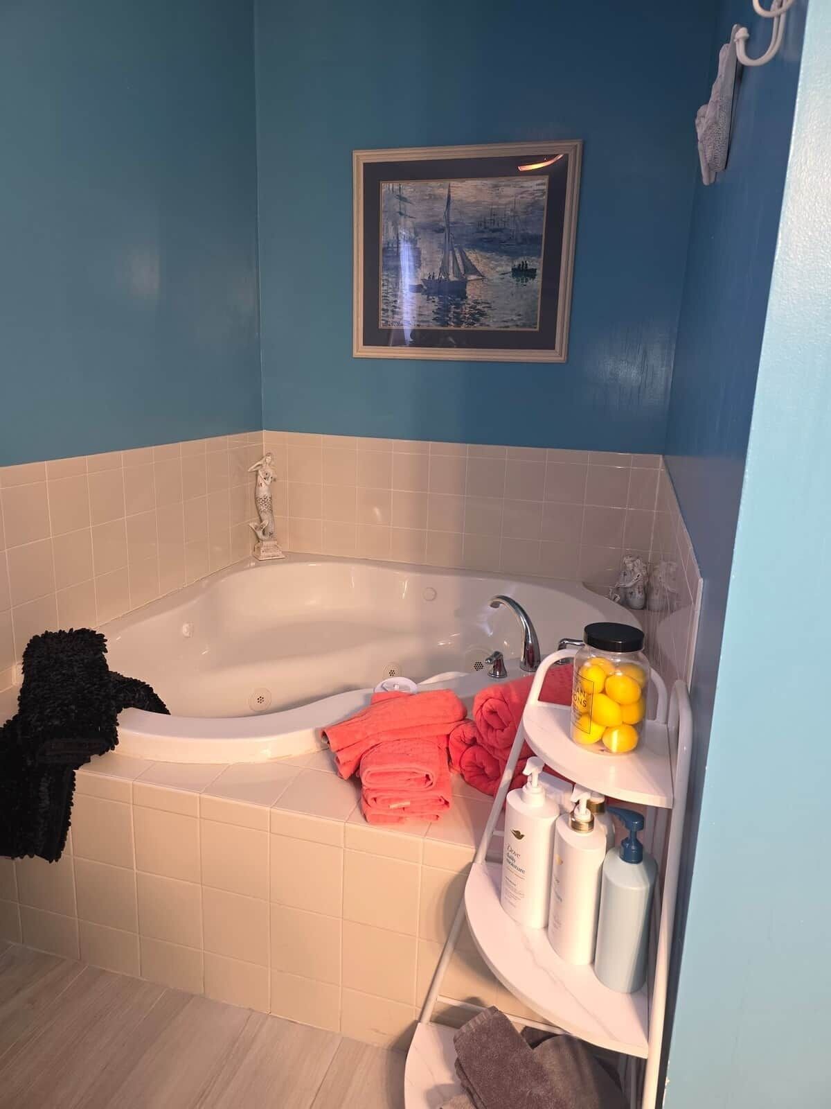 A bathroom with a bathtub, towels, toiletries, and a framed picture on the wall.