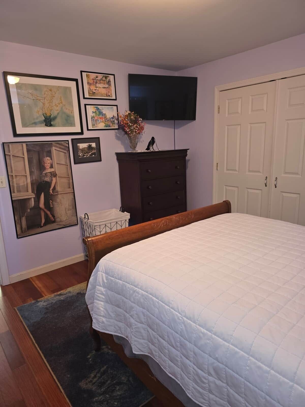 A bedroom with a bed, dresser, and wall-mounted TV.