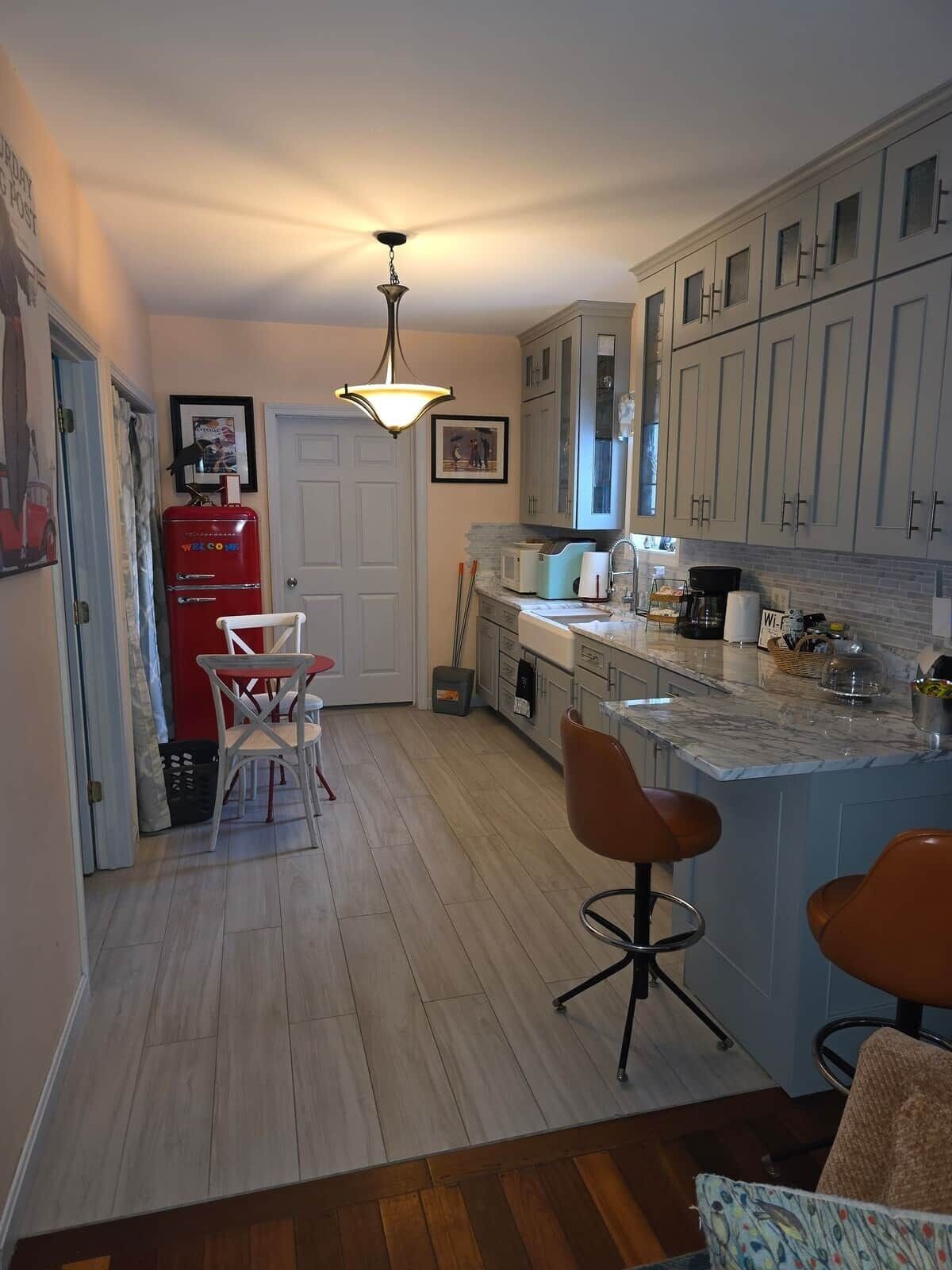 A kitchen with a marble countertop, a red refrigerator, and a dining area with two chairs.